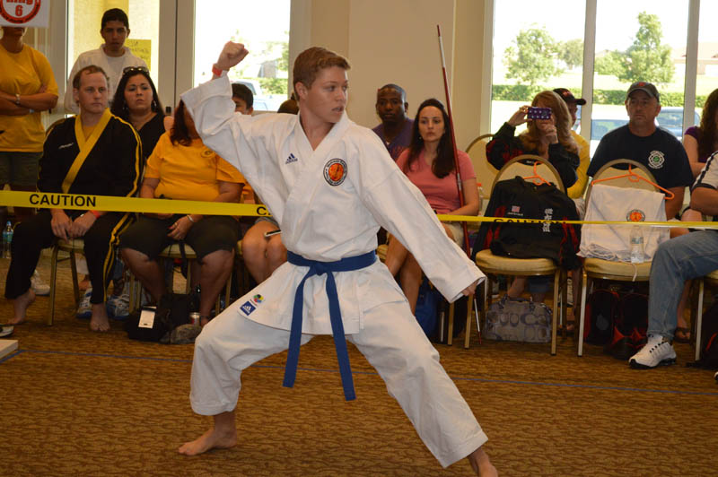 teenage boy in uniform with blue belt performs martial arts routine